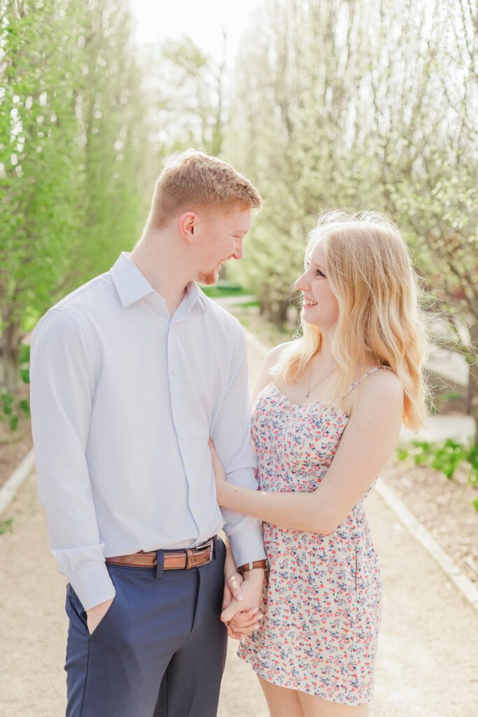 A couple looking at each other smiling while walking through the line of trees at one of the best engagement session locations in Columbus - Franklin Park Conservatory