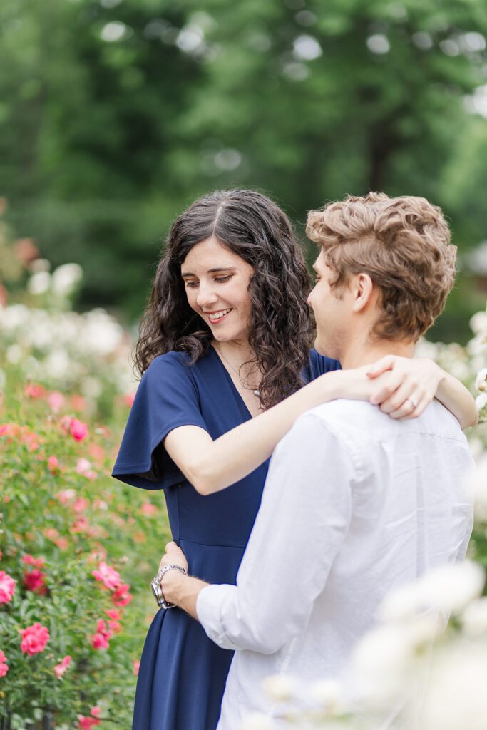 Columbus Park of Roses Engagement Photo – A couple walks hand in hand through vibrant rose gardens at the Columbus Park of Roses.