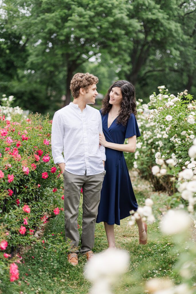 Columbus Park of Roses Engagement Photo – A couple walks hand in hand through vibrant rose gardens at the Columbus Park of Roses, one of the best engagement session locations in Columbus.